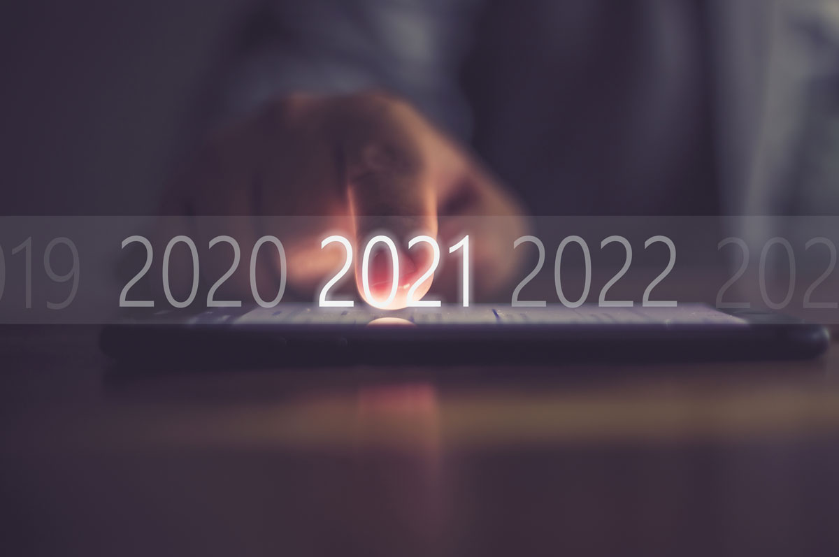 Im Hintergrund eine Hand, die auf ein Tablet zeigt und im Vordergrund leuchtet die Zahl 2021 auf einem Zeitstrahl.